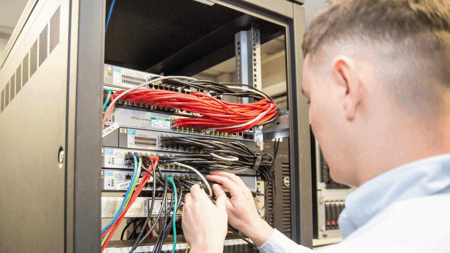 Man inspecting server cabinet with lots of red wires.